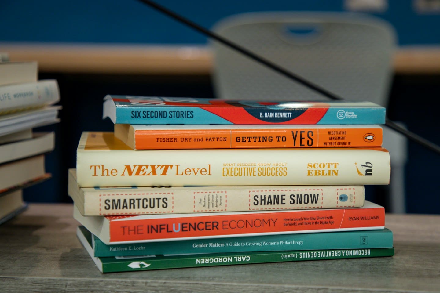 Pila di libri di business e self-help su un tavolo di legno chiaro.