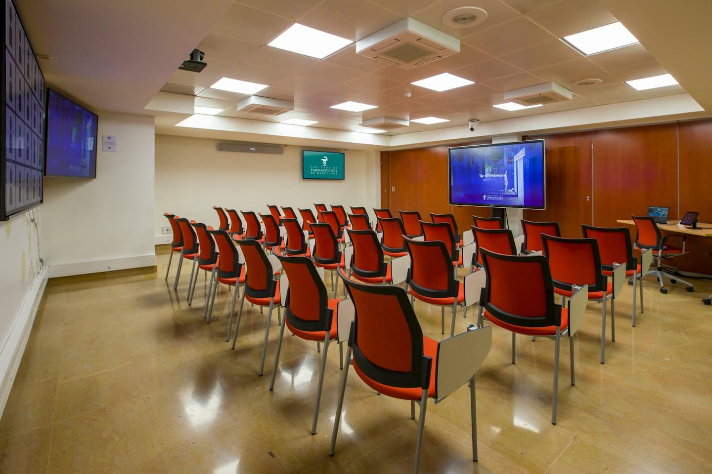 Sala conferenze moderna con file di sedie rosse e tavolette per scrivere.