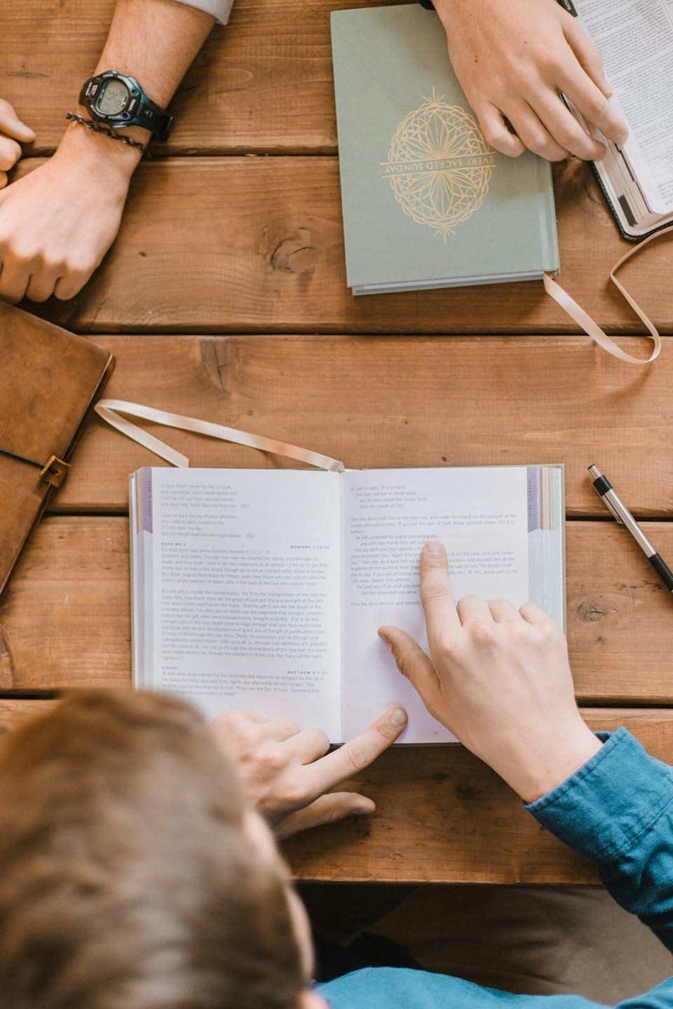 Persone che discutono un libro attorno a un tavolo rustico di legno.