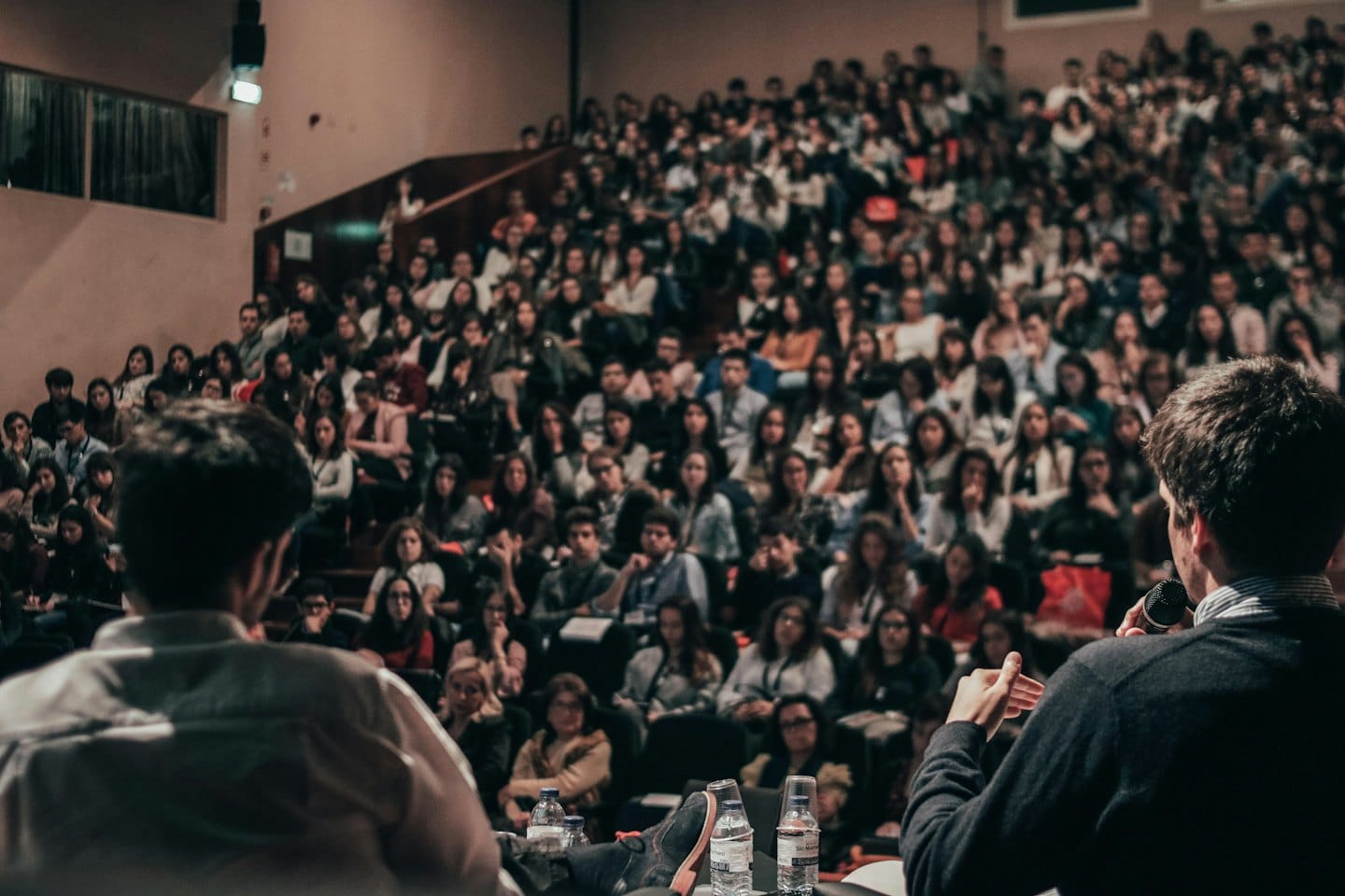 Relatori sul palco che presentano a un vasto pubblico in un auditorium.
